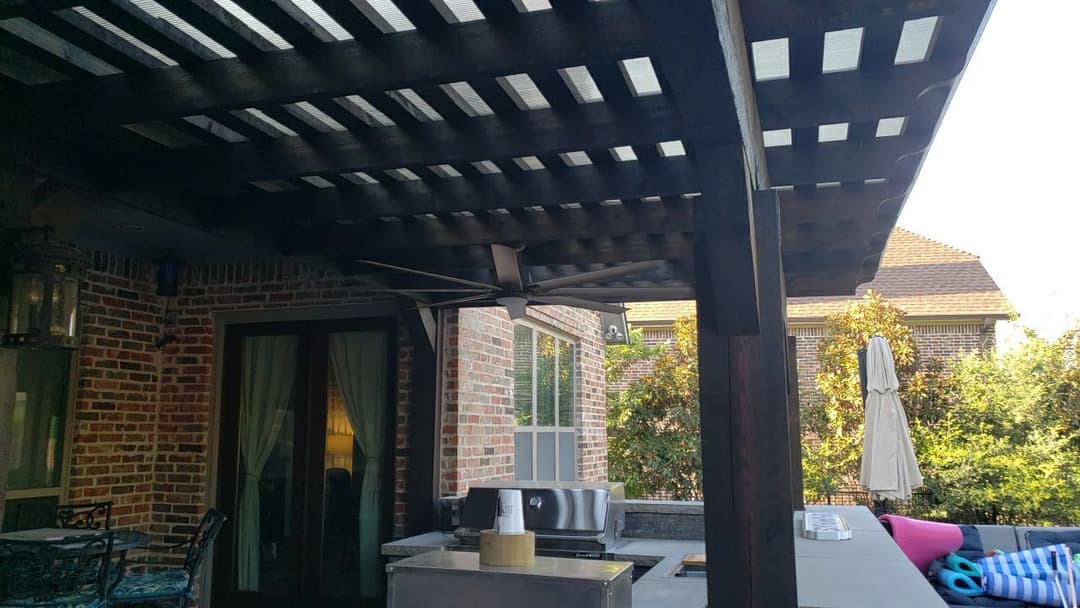 Covered outdoor patio with ceiling fan, grilling area, and seating under a wooden pergola.