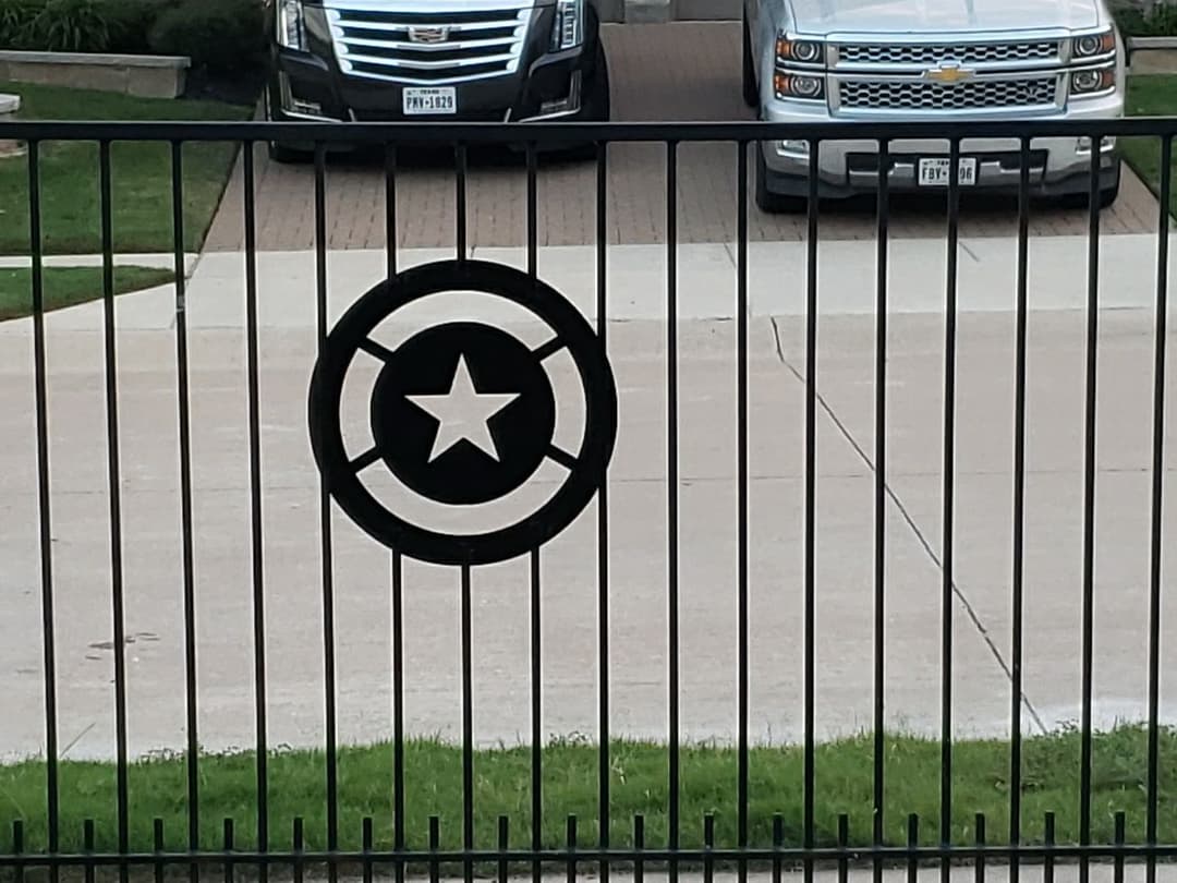 Wrought iron gate featuring a star emblem, with parked cars in a driveway.