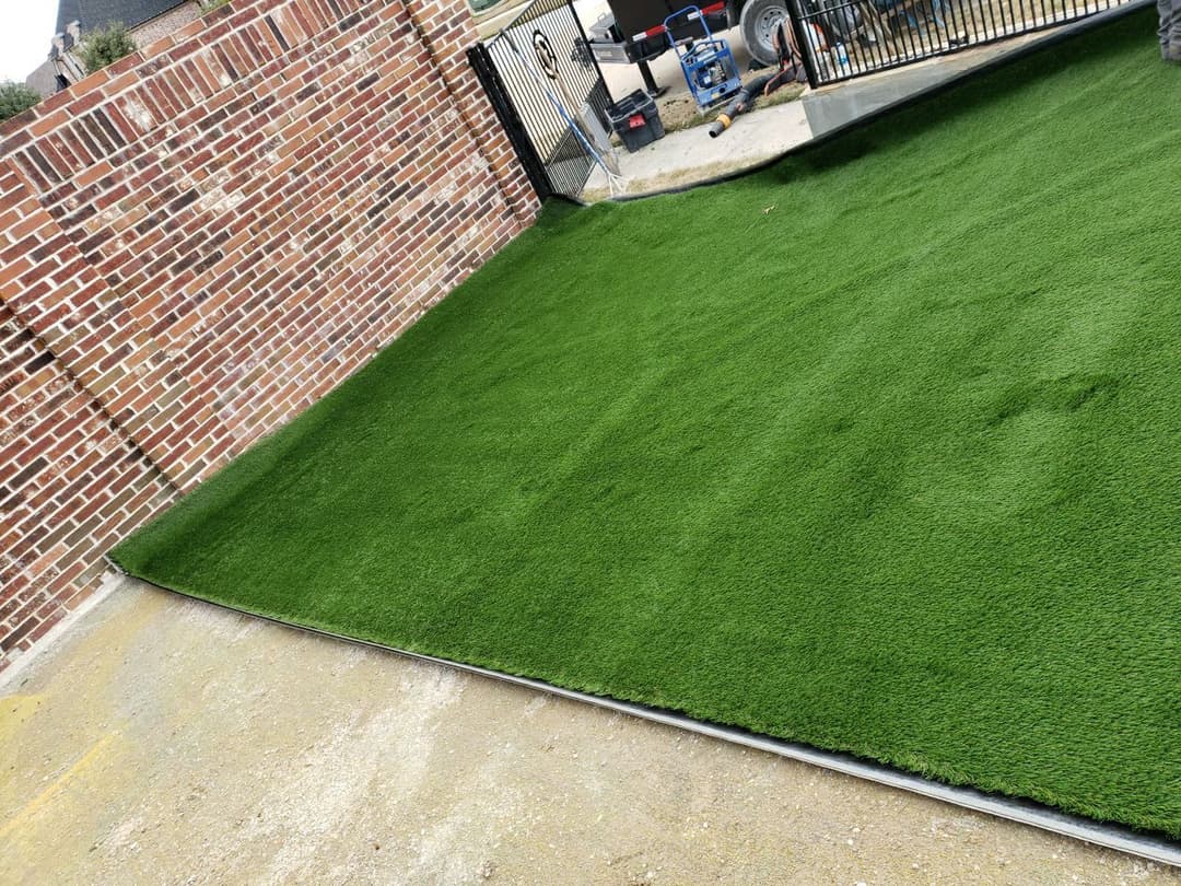 Lush green artificial grass installation alongside a brick wall and driveway.