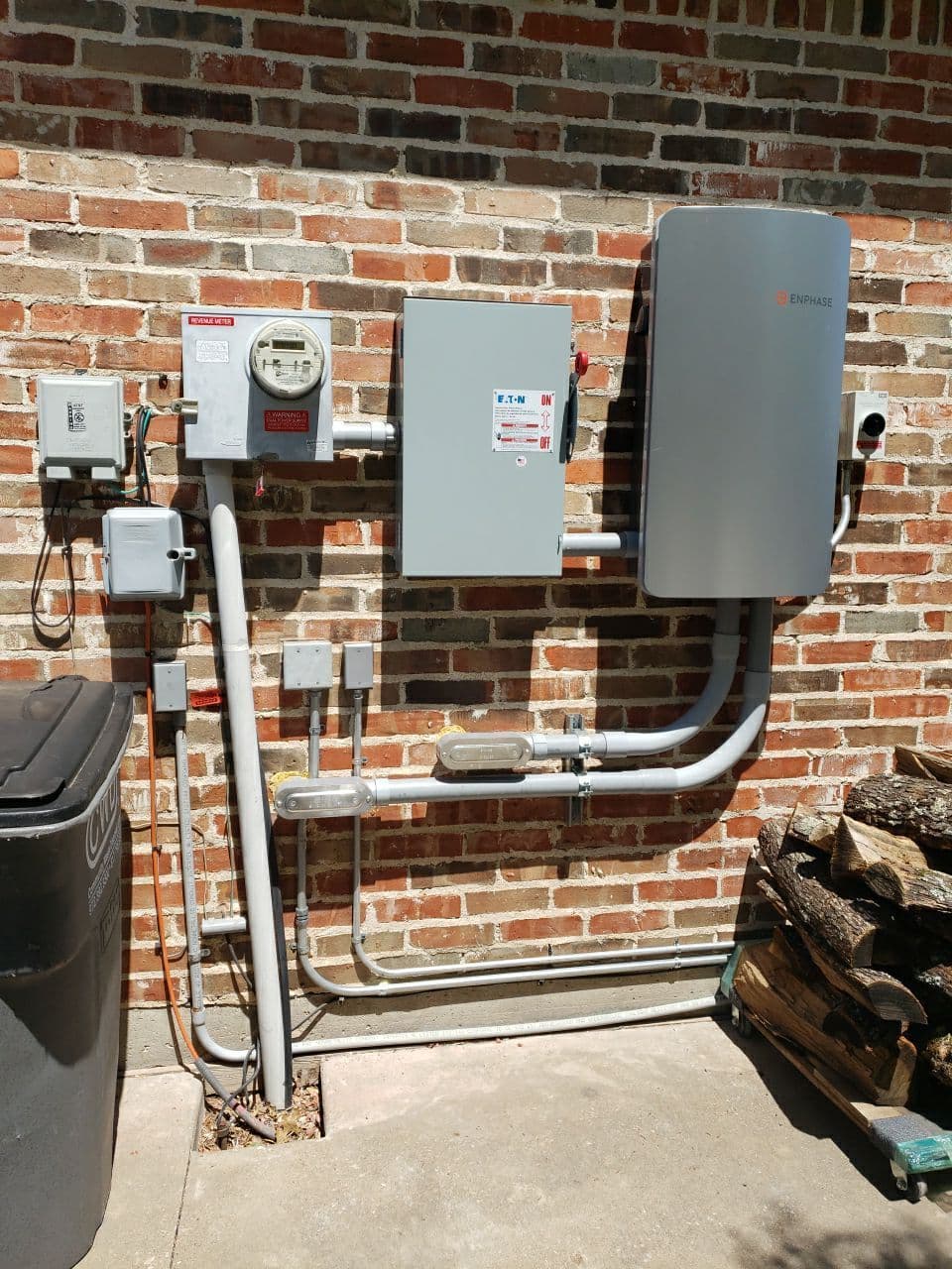 Enphase energy system installation on a brick wall with utility meter and pipes.