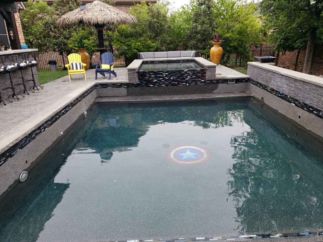 Backyard pool with star emblem, surrounded by chairs and lush greenery. Modern outdoor design.