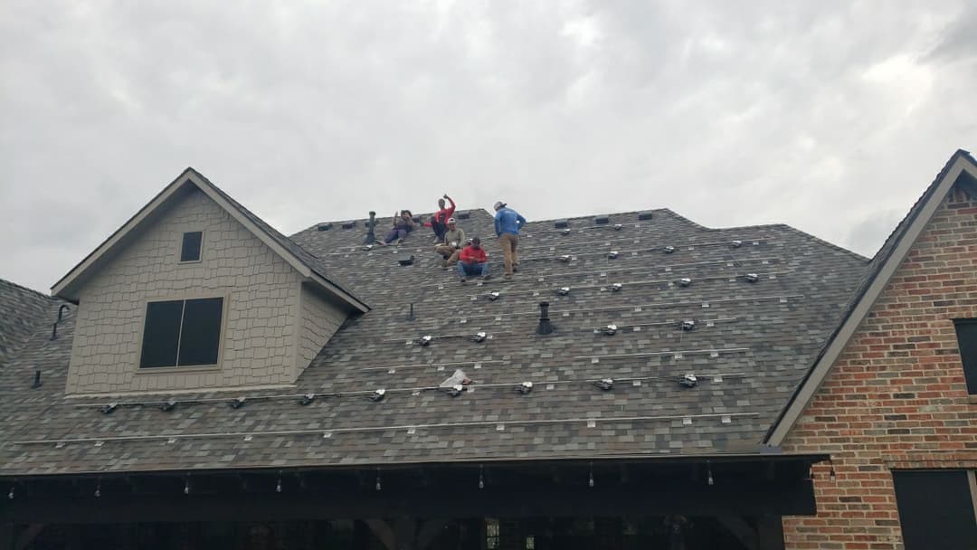 Roofing crew installing shingles on a residential home under overcast skies.