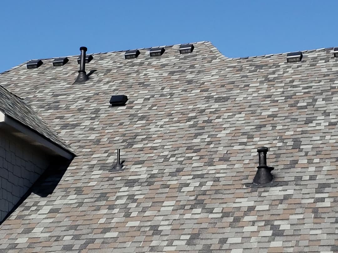 Residential roof with asphalt shingles, vents, and clear blue sky.