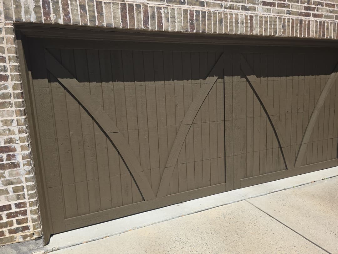 Brown wooden garage door with diagonal planks on a brick wall.