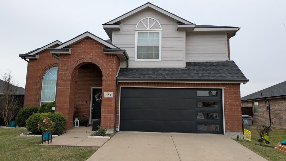 Two-story brick home with a modern black garage door and a landscaped front yard.