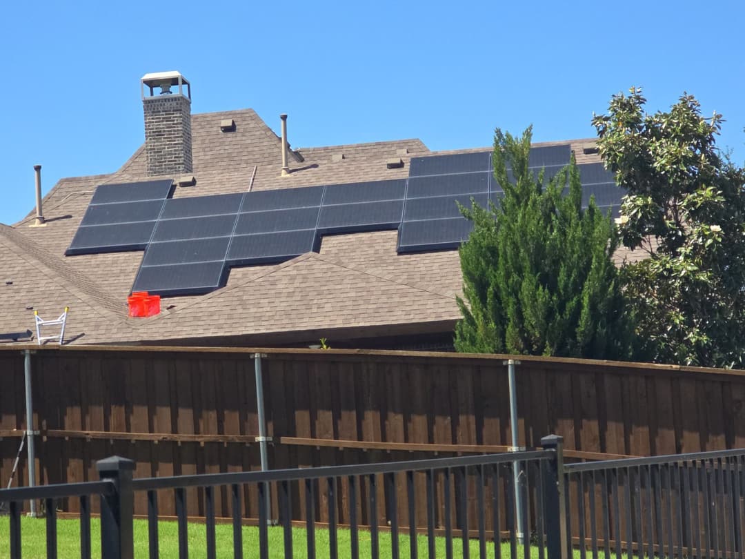 Solar panels installed on a roof of a suburban home with a clear blue sky background.