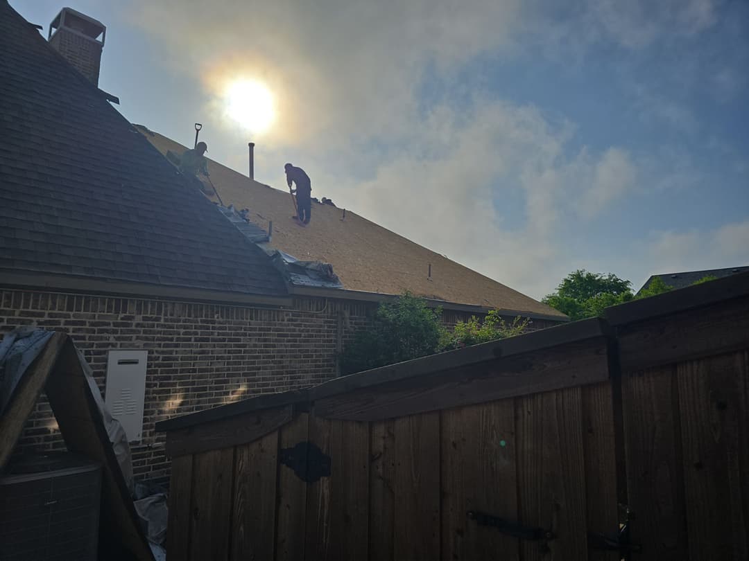 Workers installing roofing on a house under a sunny sky with clouds.