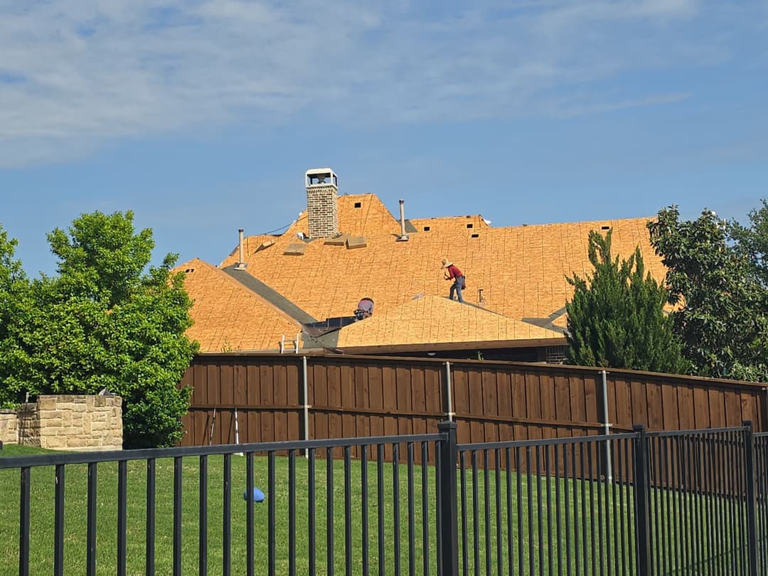 Roofers installing shingles on a residential home under a clear blue sky.