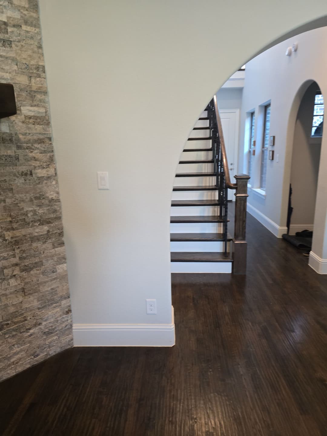 Interior view of a modern home featuring a staircase, stone wall, and hardwood flooring.