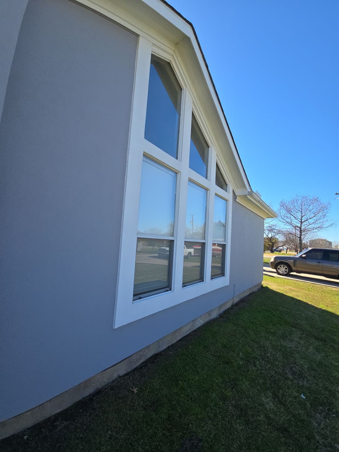 Modern gray house exterior with large windows and green lawn under a clear blue sky.