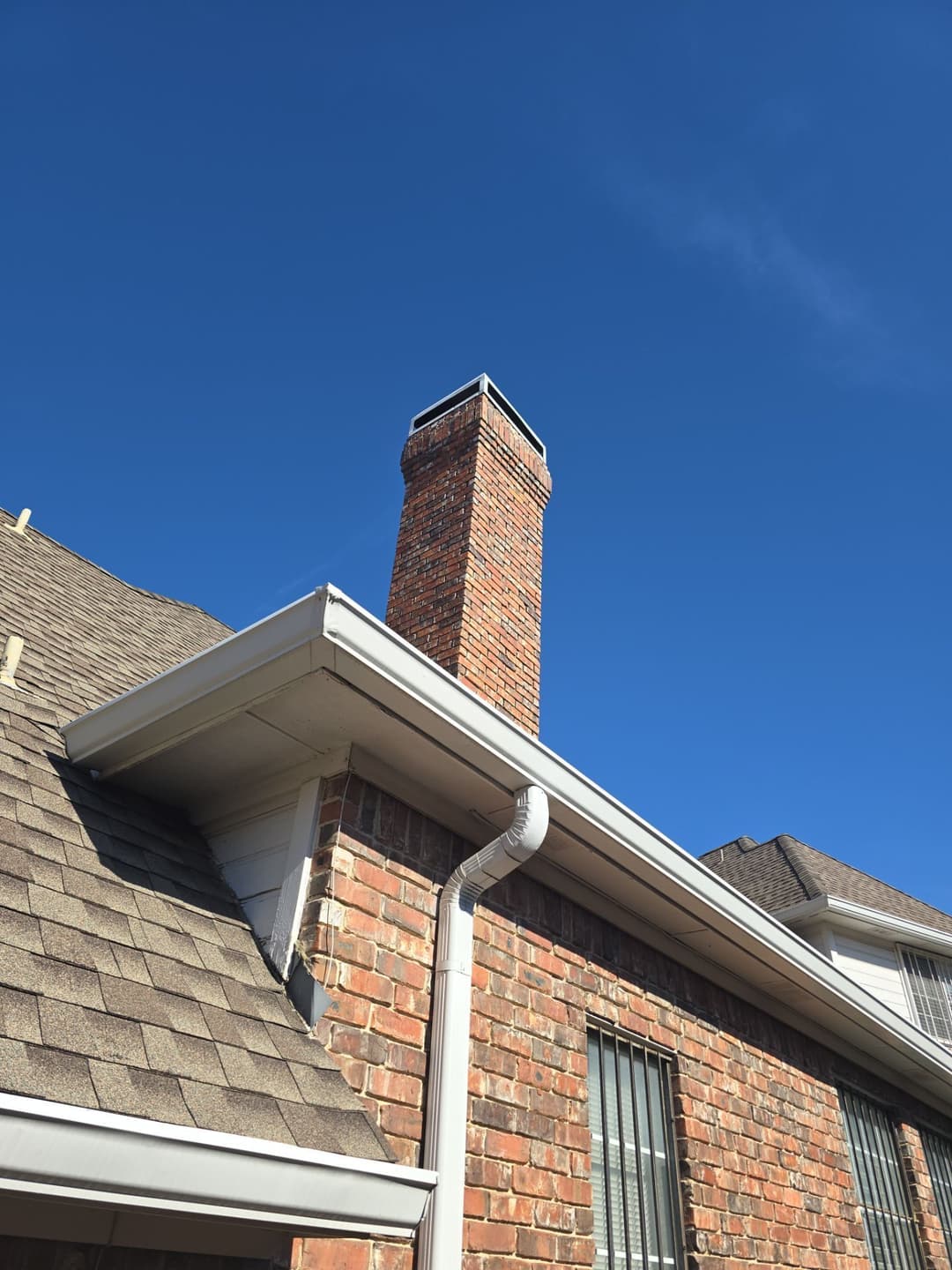 Brick chimney on a home under a clear blue sky with a sloped roof and gutter.