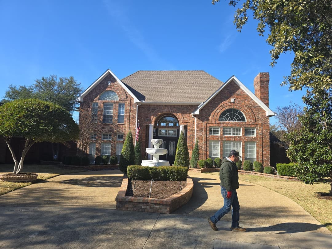 Brick house with landscaped garden, fountain, and person walking along the driveway.