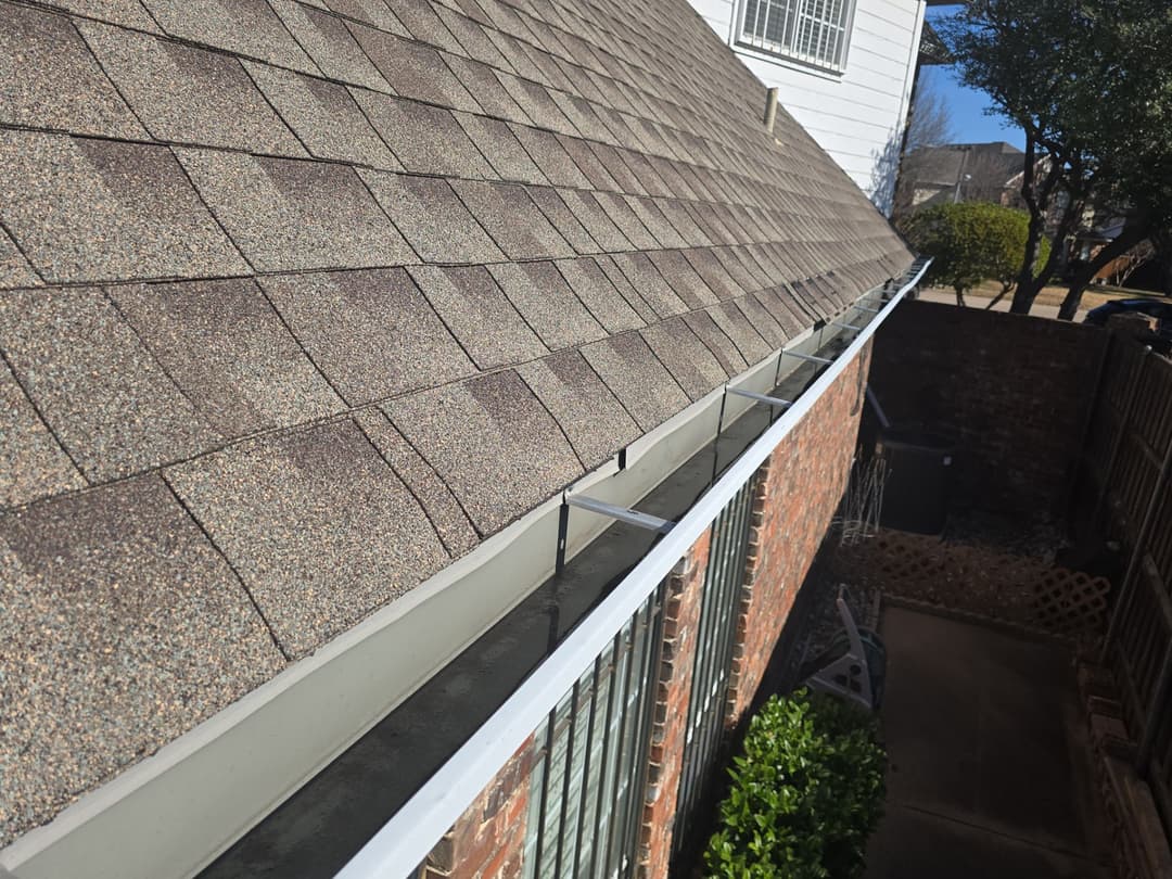 Roof with asphalt shingles and gutter system on a residential home. Bright daylight setting.