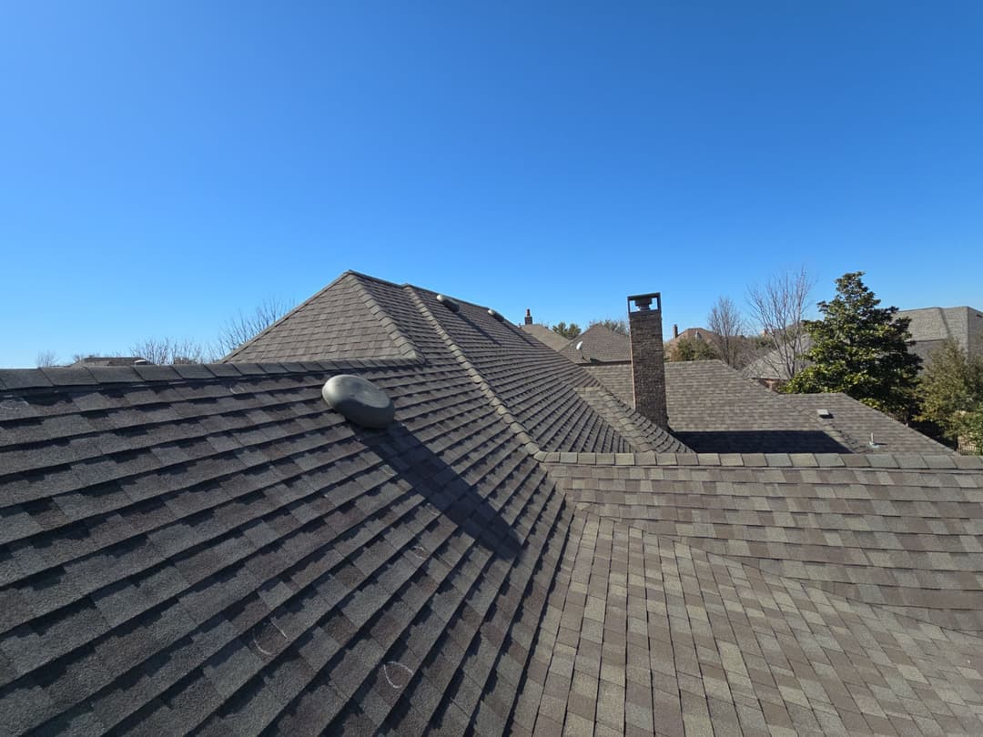 Aerial view of residential roofs with shingles under a clear blue sky.