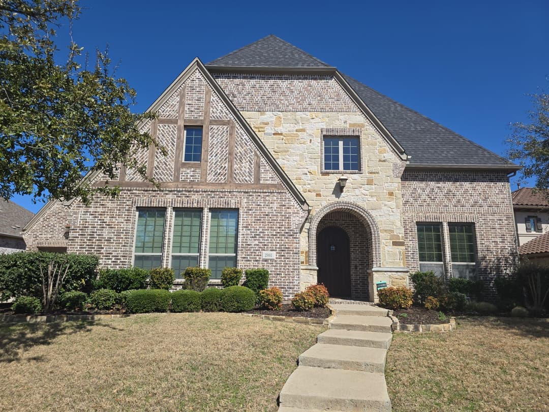 Elegant two-story brick home with stone accents, well-maintained landscaping and clear blue sky.
