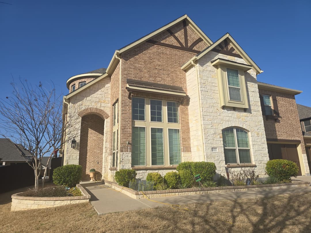 Two-story suburban home with stone exterior, large windows, and well-manicured lawn.