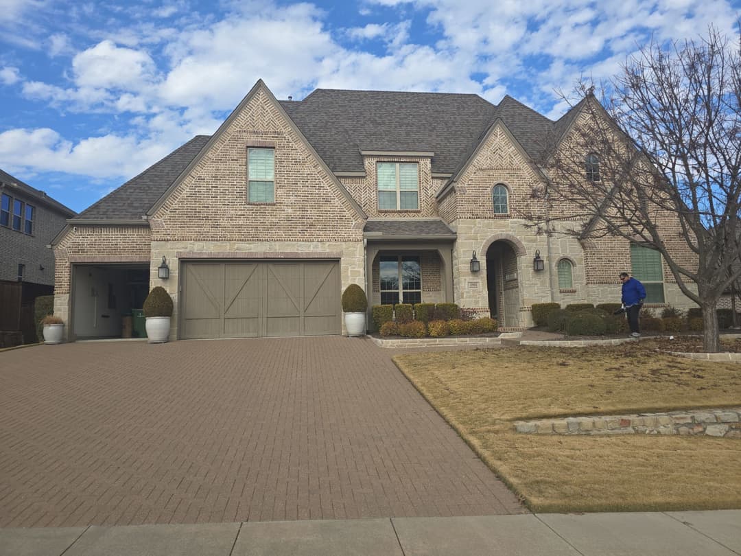 Elegant brick home with gabled roof, landscaped yard, and two-car garage under a blue sky.
